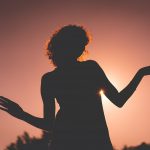 silhouette of woman raising her hands during sunset
